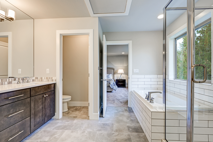 Gorgeous bathroom interior boasts drop-in tub with white tile surround next to glass shower dark wood bathroom vanity accented with mosaic backsplash. Northwest USA
