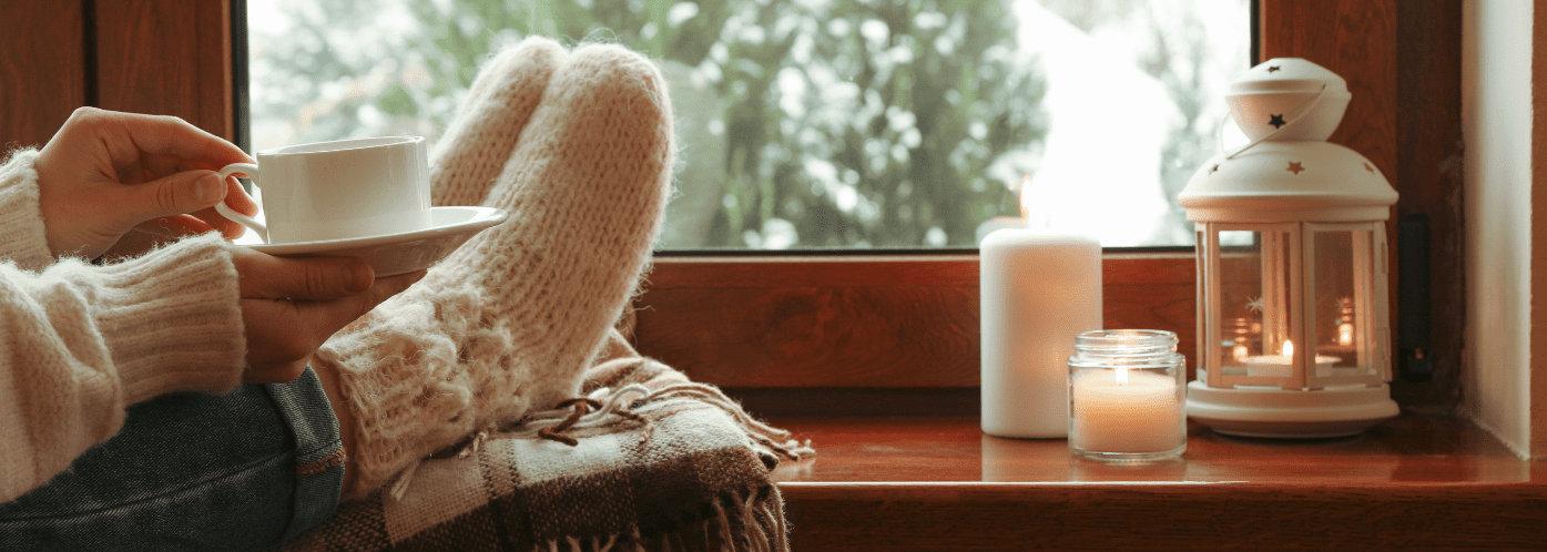 Feet on a windowsill with a cup of tea and candles
